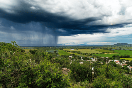 Campo agrícola ao ar livre, com uma grande nuvem de chuva se aproximando ao fundo.