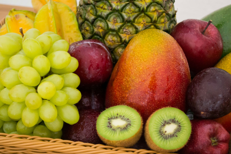 Cesta com diversas frutas frescas, incluindo maçãs, uvas, bananas, laranjas e outras frutas coloridas, organizadas em conjunto.