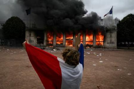Em Lyon, no sul da França, um manifestante, enrolado na bandeira do país, diante do escritório de Turismo em chamas • JEFF PACHOUD/AFP