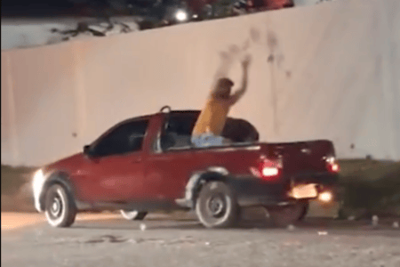 Homem na carroceria de uma caminhonete vermelha joga santinhos eleitorais pela rua.