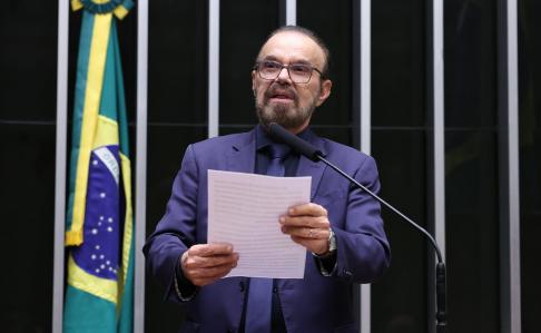 De terno, camisa e gravata em tons de azul, Lincoln Portela fala em microfone da Câmara dos Deputados enquanto segura papel