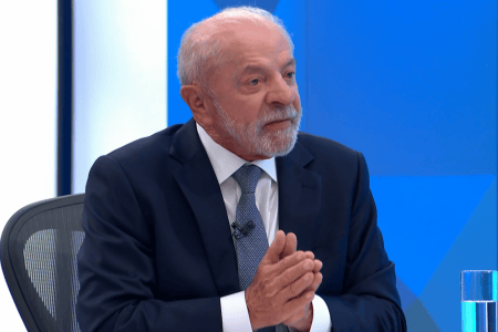 Lula, de camisa branca, gravata azul e terno preto, gesticula de mãos juntas durante entrevista na TV Globo