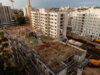 Vista de cima de um prédio em construção, profissionais estão na laje do prédio, ao fundo há outros prédios já erguidos
