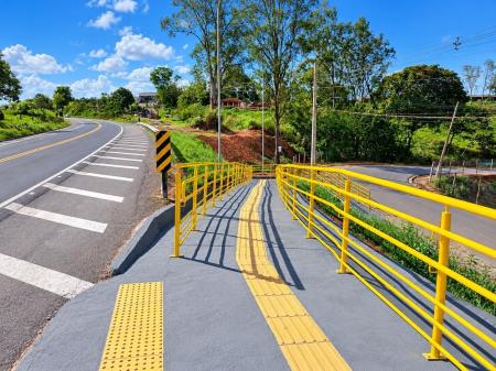 Trecho urbano de rodovia com sinalização horizontal, travessia elevada e defensas metálicas recém-instaladas.