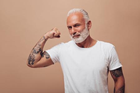 Adulto com barba grisalha e tatuagens posando para a câmera.