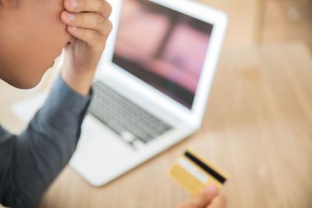 Pessoa demonstra preocupação ao analisar um cartão de crédito diante de um notebook.