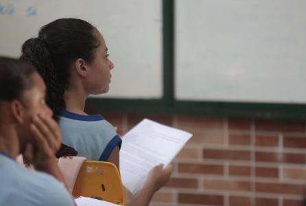 Aluna de escola brasileira segura atividade enquanto olha para a lousa