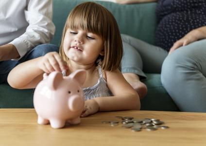 Criança coloca moedas em cofrinho com o acompanhamento dos pais.