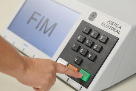 Eleitor dirigindo-se à urna eletrônica para registrar o voto na cabine de votação.