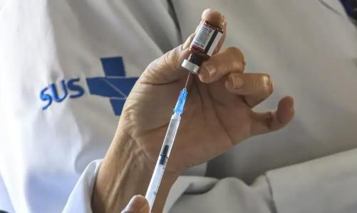 Profissional de saúde aplicando vacina em criança no braço em sala de imunização.