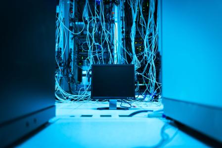 Imagem mostra uma sala com luz azul. Fios de rede estão pendurados e à frente deles uma tela de computador.