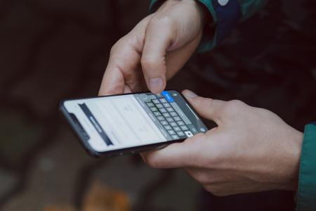 Fotografia de um homem branco segurando um smartphone com as duas mãos