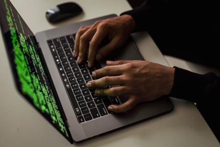 Imagem mostra duas mãos sobre o teclado de um laptop que está em cima da mesa. À direita um mouse.
