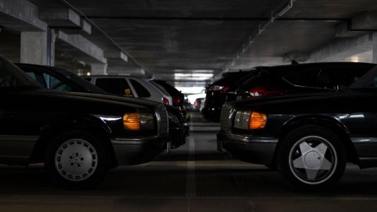 Imagem mostra garagem com carros emparelhados nas vagas. Os carros são escuros e estão de frente um para o outro