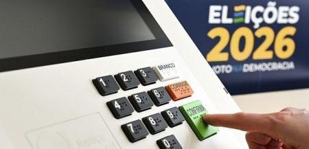 Urna eletrônica das Eleições 2026 com a mão de um eleitor apertando a tecla "Confirma".